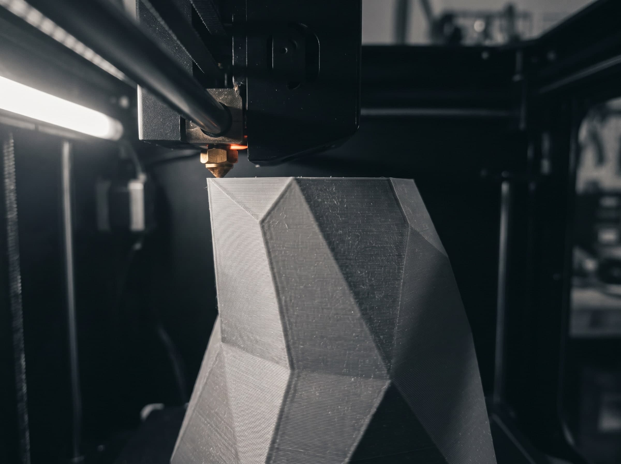 Düse eines 3D-Druckers legt eine Schicht auf ein kantiges graues Objekt